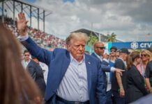Man in blue suit waving in a crowd outdoors