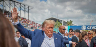 Man in blue suit waving in a crowd outdoors