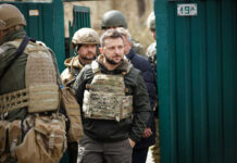 Men in military gear in front of green gate.