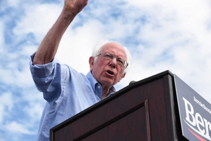 bernie-sanders-347336174 Man speaking at a podium under cloudy sky.