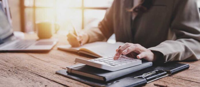 calculating personal taxes_2190783443.jpg Person calculating taxes with a calculator and writing notes in a notebook at a desk