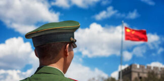 Soldier in a green military uniform facing the Great Wall of China with the Chinese flag in the background