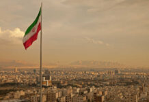 Nuclear Breakout ONE WEEK Away—Strikes Escalate Iranian flag waving over a city skyline with mountains in the background