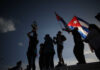 Silhouetted figures holding a trophy and Cuban flags during a celebration