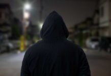 A person wearing a hooded sweatshirt standing in an urban area at night