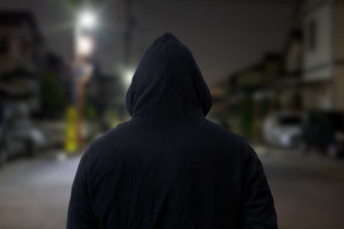 shutterstock_2181989319.jpg A person wearing a hooded sweatshirt standing in an urban area at night