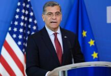Government official speaking at a podium with flags in the background