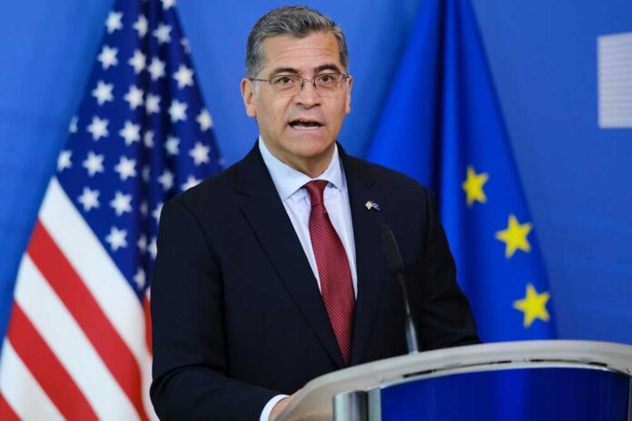Government official speaking at a podium with flags in the background