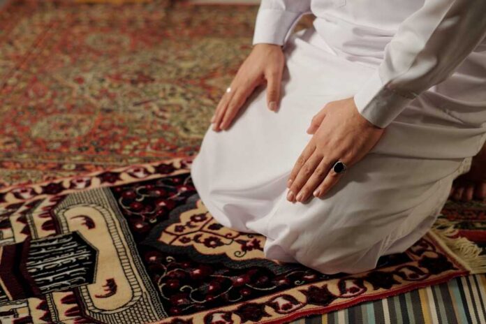 Person kneeling on a prayer rug in traditional attire