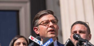 A man speaking at a press conference surrounded by microphones