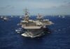 An aircraft carrier surrounded by various naval vessels in the ocean