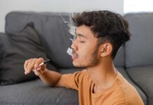 Young man sitting on a couch, vaping with smoke around him