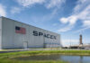 SpaceX facility with American flag and rocket launch structure in the background