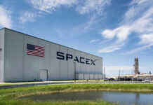 SpaceX facility with American flag and rocket launch structure in the background