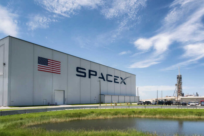 SpaceX facility with American flag and rocket launch structure in the background