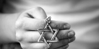 A hand holding a silver Star of David pendant