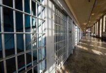 Interior view of a prison corridor with jail cells and sunlight streaming through windows