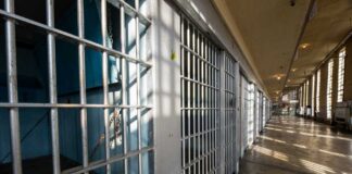 Interior view of a prison corridor with jail cells and sunlight streaming through windows