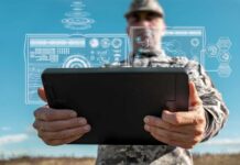A soldier holding a tablet displaying digital data overlays