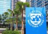 Sign of the International Monetary Fund in front of a modern building with palm trees