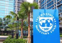 Sign of the International Monetary Fund in front of a modern building with palm trees
