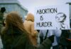 Person holding a sign that reads 'Abortion is Murder' at a protest