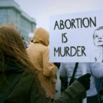 Person holding a sign that reads 'Abortion is Murder' at a protest