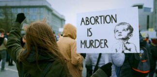Person holding a sign that reads 'Abortion is Murder' at a protest