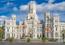 A grand historic building with flags in front and a fountain