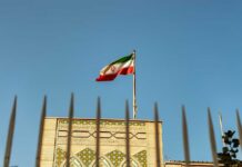 UN Prepares for Nuclear Fallout in Iran Iranian flag waving above a government building against a blue sky