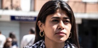 A woman with long hair wearing a patterned scarf, looking thoughtfully into the distance