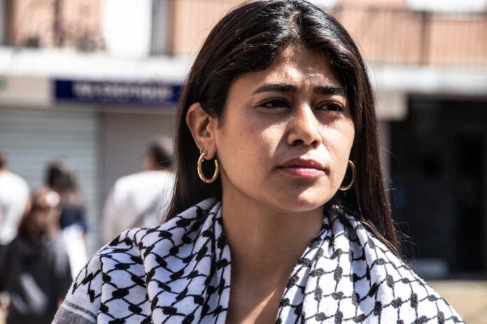 A woman with long hair wearing a patterned scarf, looking thoughtfully into the distance