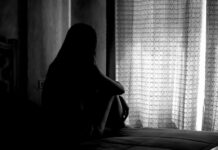Silhouette of a person sitting on a bed near a window with light filtering through curtains