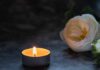A lit candle beside a white flower on a dark surface