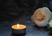 A lit candle beside a white flower on a dark surface
