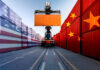 Tense Truce: US-China Trade Game Unveiled! Container handler lifting orange shipping container between flag-painted stacks