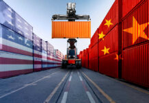Container handler lifting orange shipping container between flag-painted stacks