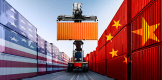 Container handler lifting orange shipping container between flag-painted stacks