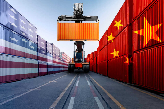 Metaphor,Image,Of,United,States,Of,America,And,China,Trade Container handler lifting orange shipping container between flag-painted stacks
