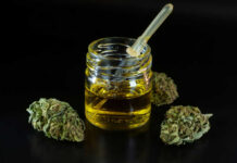 Glass jar of cannabis oil with dropper and dried buds