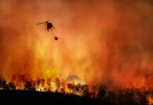 Helicopter fighting wildfire over burning forest at dusk
