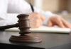 Wooden judge's gavel on a desk with a person writing in the background