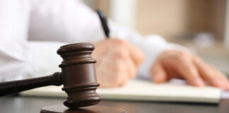 Wooden judge's gavel on a desk with a person writing in the background