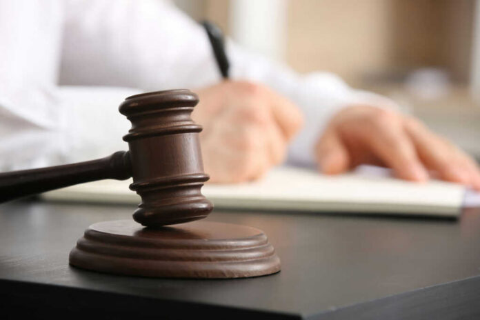 Wooden judge's gavel on a desk with a person writing in the background