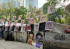 Street protest camp with rows of missing persons posters on a barricade