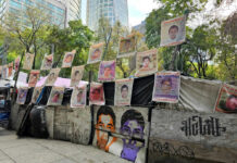 Street protest camp with rows of missing persons posters on a barricade