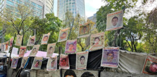 Street protest camp with rows of missing persons posters on a barricade