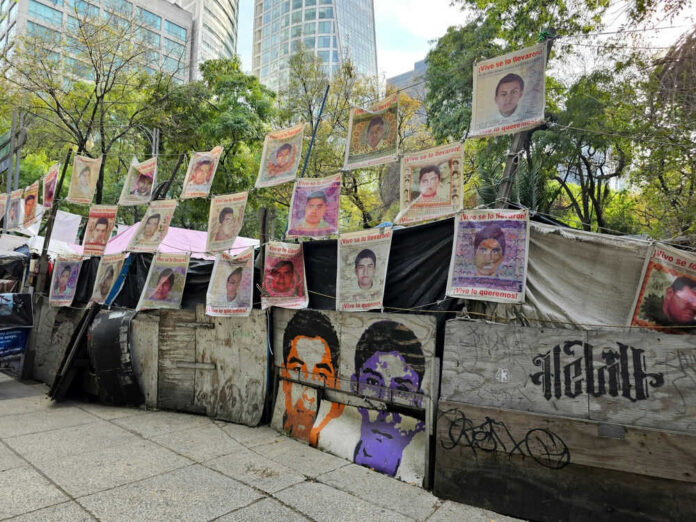 Street protest camp with rows of missing persons posters on a barricade