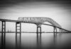 A large bridge spanning over a calm body of water in black and white