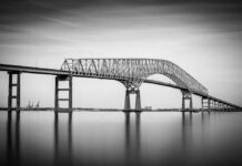 A large bridge spanning over a calm body of water in black and white